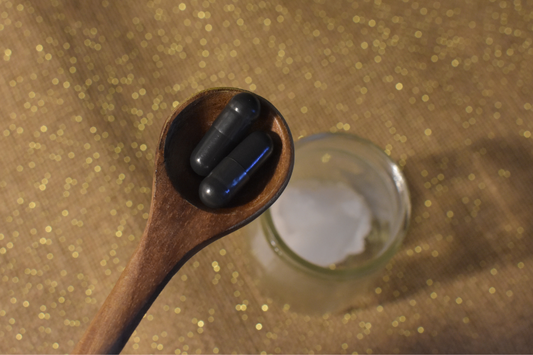 wooden spoon with activated charcoal capsules and a small jar of coconut oil
